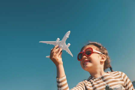 Little girl with toy plane in her hands against blue sky