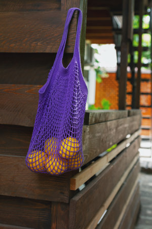 yellow lemons in purple string bag hangs on wooden terrace