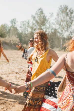 young smiling woman hippie in ethnic costume dancing american flag in hands between other women, selective focus, film noiseの写真素材