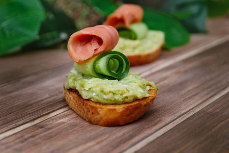 sandwich with guacamole, cucumber and red fish on wooden table on monstera leaves