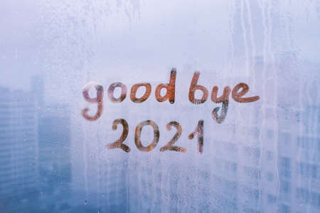 Handwritten lettering good bye and orange arabic numerals 2021 on misted glass on blue window flooded with raindrops on sunny backgroundの写真素材