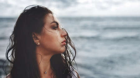 portrait of brunette woman in profile looks to right with wet flying hair against background of seaの写真素材