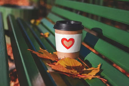 cup of coffee with carved orange heart and yellow autumn maple leaves on green bench, copy spaceの写真素材