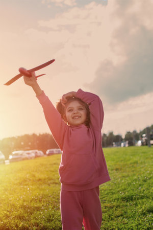 happy girl in pink sportswear with red toy plane running on green grass in sunny summerの写真素材