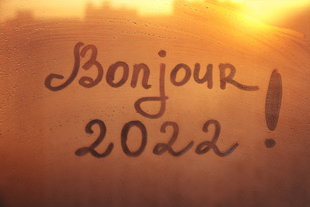 lettering Bonjour in French is hello in english and numbers 2022 paint with finger with streaks of water on splashed by rain foggy glass on orange sunset windowの写真素材