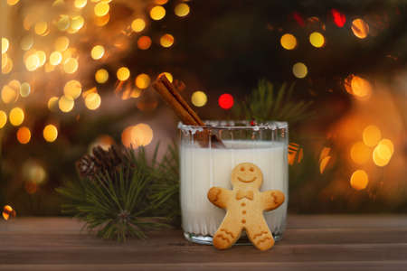 gingerbread man with glass of eggnog on wooden brown table with spruce branches and orange lights bokeh, selective focusの写真素材