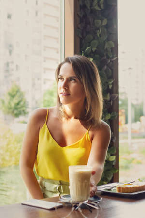 portrait of smiling woman in yellow clothes with glass of coffee latte