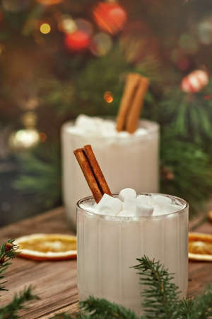 white eggnog in glass and cream on wooden brown table with spruce branches and dried orange slices, selective focusの写真素材