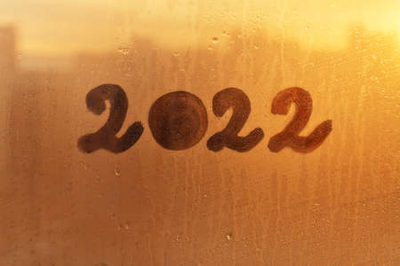 numbers 2022 of new year paint with finger on splashed by rain foggy glass on orange sunset windowの写真素材