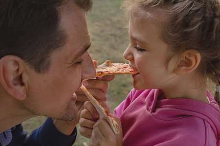 little girl and her dad feed each other pizza and laughの写真素材