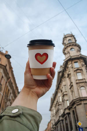 paper cup of natural coffee in womans palm on background of building in St. Petersburg
