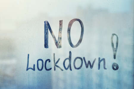 Handwritten lettering NO lockdown drawn on misted glass on blue window flooded with raindrops on blue cloudy backgroundの写真素材