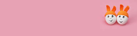 banner two white eggs in orange beanie with rabbit ears and cheerful faces on pink background, copy...