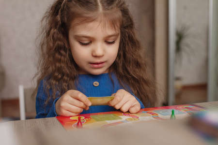 portrait of little girl 5 years old with interest looks at board game