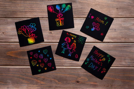 children's multi-colored drawings on black sheets for notes on a wooden table, mothers day