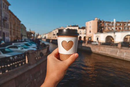 paper cup of natural coffee in womans palm on background of river in city St. Petersburgの写真素材