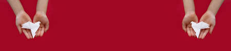 banner two white paper origami pigeon in children's hands on red background, copy space