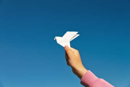 white paper origami pigeon in children's fingers on blue sky background, copy spaceの写真素材