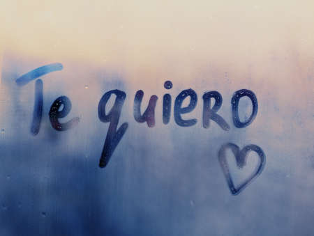 Handwritten message in Spanish language Te quiero words I love you in english and hand drawn heart on misted glass on blue window flooded with raindropsの写真素材