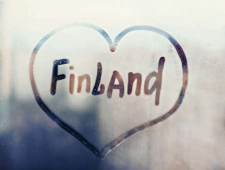 Handwritten word Finland in heart shape on misted blue window with raindrops against background of outlines of urban housesの写真素材