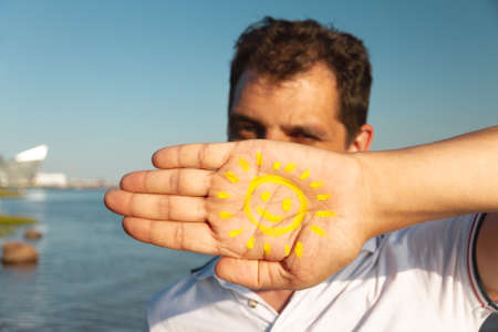 mens one palm with painted yellow smiling face on blue sky bakground, world smile day concept, selective focusの写真素材