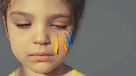 sad girl 5 years old with yellow and blue flower petals under her left eye like flag of ukraine