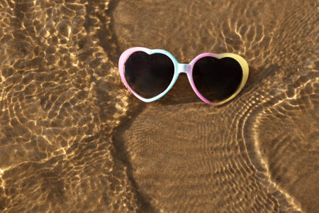 heart shaped multi-coloured sunglasses on beach sand washed by the seaの写真素材