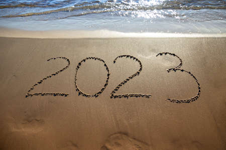 Hand-drawn numbers 2023 of new year on wet yellow sand on beach, copy spaceの写真素材