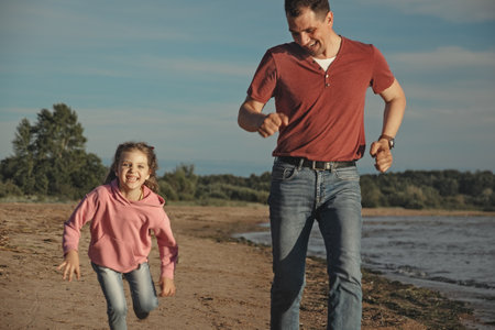 happy little daughter of 5 years runs with her dad on beach at sunset, selective focusの写真素材