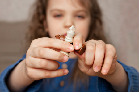 two white and brow wooden chess queen in finger of little girl, close-up, selective focus, games for children, learning chess game, leisureの写真素材