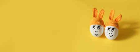 two white eggs in orange beanie with rabbit ears and cheerful faces on yellow backgroundの写真素材