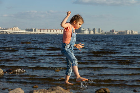 Happy child girl of 4 years in dress on summer beach walks on sea water, lifestyle, copy spaceの写真素材