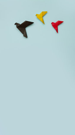 three paper origami pigeons black, yellow, red on light blue background, vertical, 16:9の写真素材