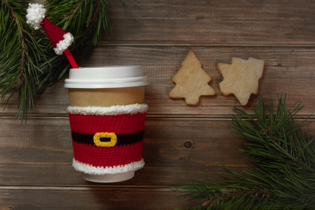 flat lay christmas paper beige cups with white lid dressed in red santa claus clothes on wodden background with fir branches and Christmas tree cookies, selective focusの写真素材