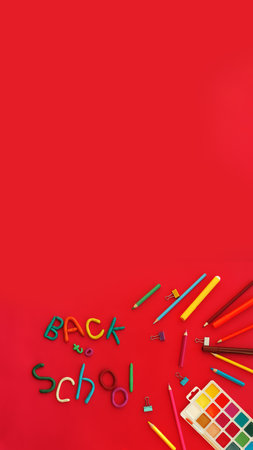 vertical banner lettering of multi-colored plasticine back to school in wry funny style and school supplies felt-tip pens, paints, pen, paper clips, on red background, copy spaceの写真素材