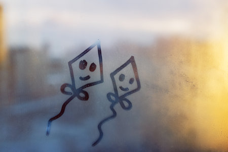 Two happy smile doodle kite painted on blue and orange window flooded with raindrops on background of cityの写真素材