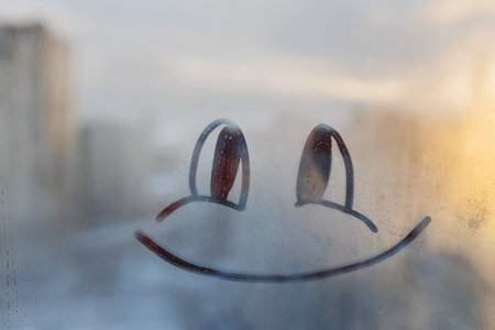 Happy smile doodle painted on sunset window flooded with raindrops on background of cityの写真素材
