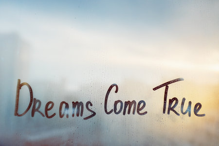 Handwritten message wish Dreams come true on misted glass on sunset window with raindropsの写真素材