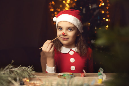 6 years old girl in Santa Claus costume hugging paints his nose red and festive lights on backgroundの写真素材