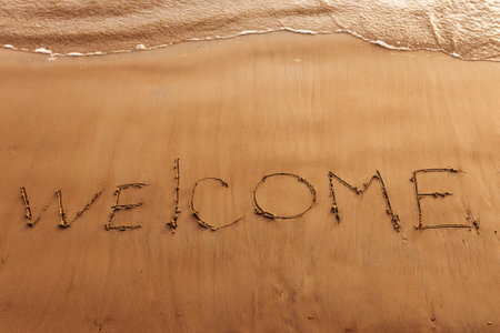 Hand drawn message Welcome on wet yellow sand on beach of seaの写真素材