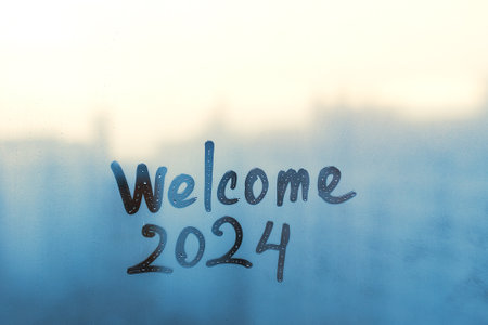 lettering Welcome and numbers 2024 of new year paint with finger on splashed by rain foggy glass on blue and sunset windowの写真素材
