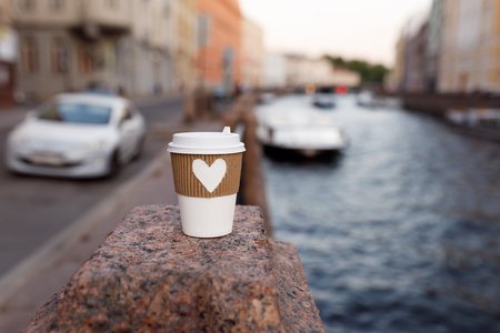 white cup of natural coffee with carved brown heart on bridge near embankment of Fontanka river in St. Petersburgの写真素材
