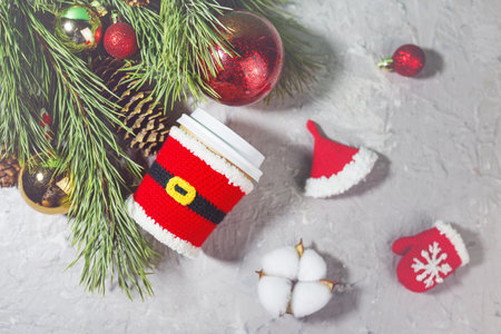 christmas paper beige cups with white lid dressed in santa claus clothes on gray background with fir branches and Christmas tree decorsの写真素材