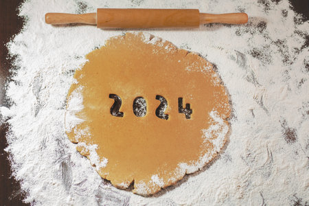 2024 numbers cut from rolled raw cookie dough on flour brown table and rolling pin
