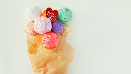 Gift bouquet of multi-colored balls of yarn in craft packaging and red wooden heart with wish happy...