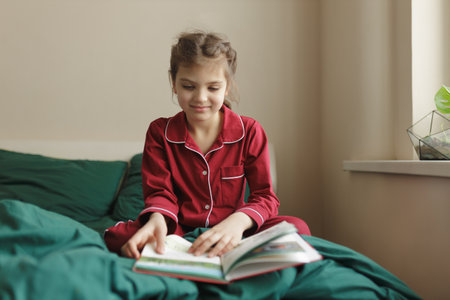Girl in homemade pajamas sitting in bed and reading book, lifestyle.の写真素材