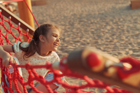 Happy real cheerful 8 year old girl swinging in red hammock on beach on sunny day, life styleの写真素材