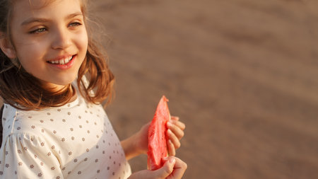Happy smiling girl holds slice of ripe red watermelon in summer on beach on bench, copy space, bannerの写真素材