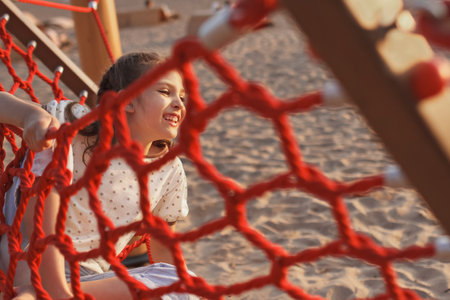 Happy smiling cheerful 8 year old girl swinging in red hammock on beach