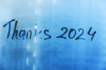 lettering Thanks and numbers 2024 paint on splashed by rain foggy glass on blue windowの写真素材